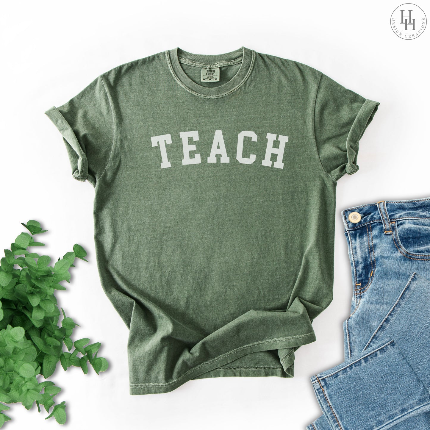 Moss green t-shirt with 'TEACH' printed on it, placed on a white background.