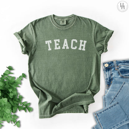 Moss green t-shirt with 'TEACH' printed on it, placed on a white background.