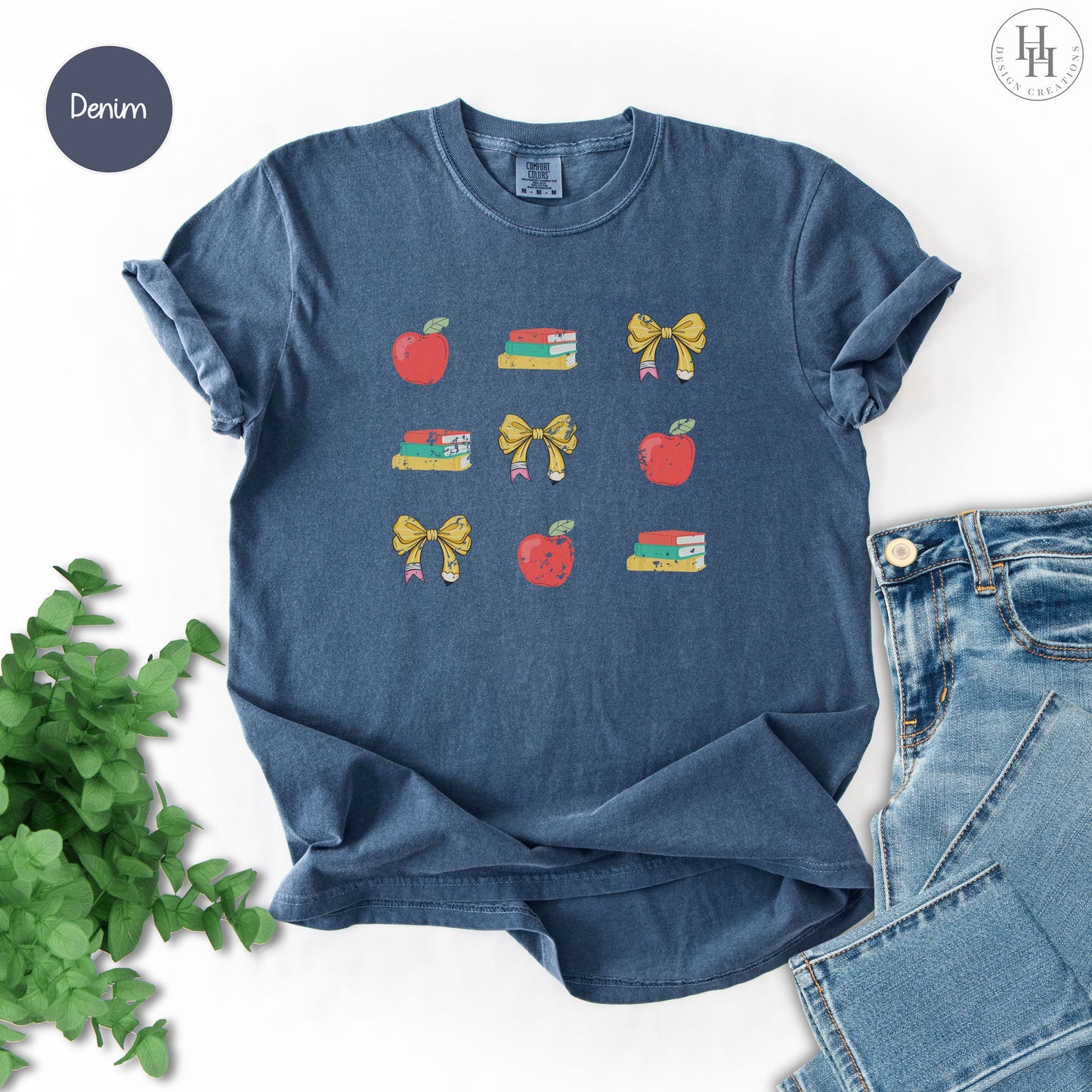Denim blue t-shirt with apple, book, and bow designs on a white background